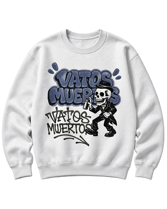 A white crewneck sweatshirt featuring a graphic print with the text 'VATOS MUERTOS' in stylized blue and black lettering, accompanied by a cartoon skeleton dressed in a black suit and top hat.